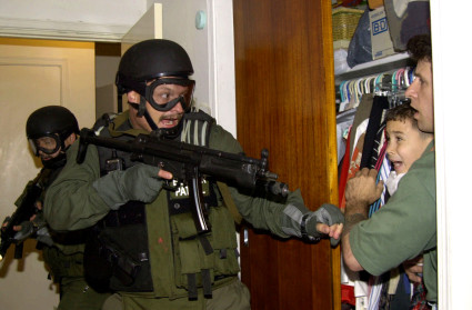 In this third of seven sequential photos, Elian Gonzalez is held in a closet by Donato Dalrymple, one of the two men who rescued the boy from the ocean, right, as government officials search the home of Lazaro Gonzalez for the young boy, early Saturday morning, April 22, 2000, in Miami. Armed federal agents seized Elian Gonzalez from the home of his Miami relatives before dawn Saturday, firing tear gas into an angry crowd as they left the scene with the weeping 6-year-old boy. Photo courtesy of AP Photo/Alan Diaz.